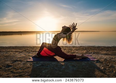 Silhouette Woman On The Beach At Sunset Doing Yoga Asana. Morning Natural Stretch Warm-up Training