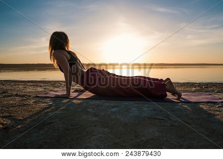 Silhouette Woman On The Beach At Sunset Doing Yoga Asana. Morning Natural Stretch Warm-up Training