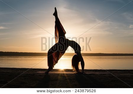 Silhouette Woman On The Beach At Sunset Doing Yoga Asana. Morning Natural Stretch Warm-up Training