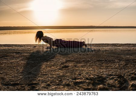Silhouette Woman On The Beach At Sunset Doing Yoga Asana. Morning Natural Stretch Warm-up Training