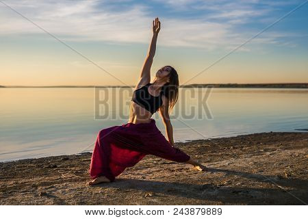Silhouette Woman On The Beach At Sunset Doing Yoga Asana. Morning Natural Stretch Warm-up Training