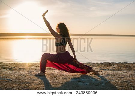 Silhouette Woman On The Beach At Sunset Doing Yoga Asana. Morning Natural Stretch Warm-up Training