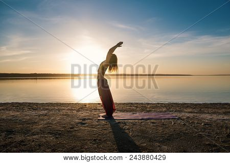 Silhouette Woman On The Beach At Sunset Doing Yoga Asana. Morning Natural Stretch Warm-up Training