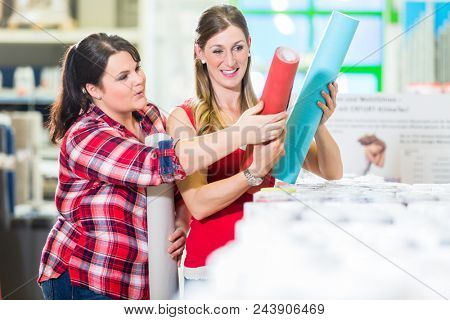 Young women in home improvement store choosing wallpapers for DIY renovating project