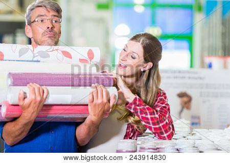 Home improving couple, woman and man, buying many rolls of wallpapers at hardware store for do-it-yourself project