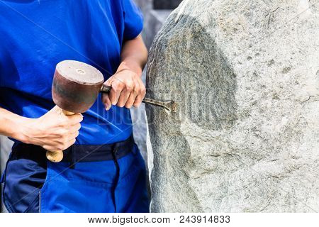Stonemason working on boulder with sledgehammer and iron in workshop
