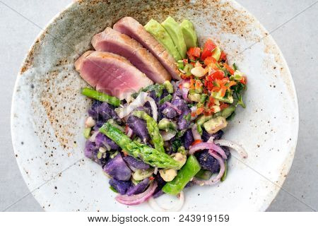 Modern fried tuna fish filet salad with green asparagus blue potatoes und vegetable chili relish as top view on a plate 
