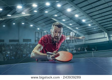 The Table Tennis Player In Motion. Fit Young Sports Man Tennis-player In Play On Sport Arena Backgro