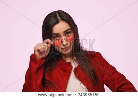 Overconfident Girl In Sunglasses And Red Jacket Looking Provocatively At Camera On Pink Background
