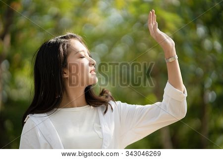 Attractive Asian Woman Raises Her Hand Enjoys The Sunlight On Her Face Feels Peaceful And Calm In Th