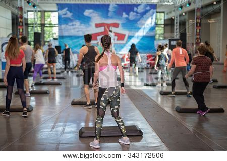 Fitness Workout In Gym: People Doing Exercises In Class With Step Platform, Music And Teacher On Sta