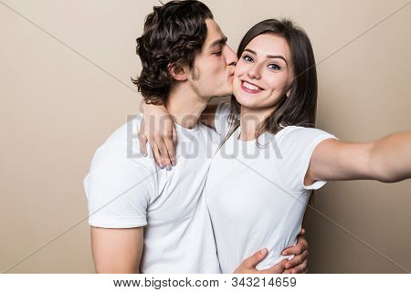 Young Couple Posing Together With Klosed Eyes While Making Selfie And Man Kissing Woman Over Beige B