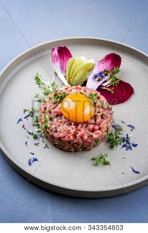Gourmet tartar raw from beef fillet with yellow of the egg and baguette as closeup on modern design dish
