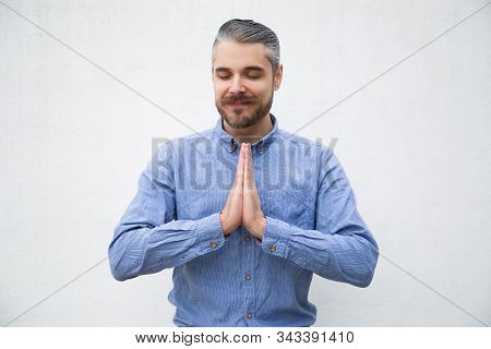 Peaceful Positive Man With Closed Eyes Making Namaste Gesture With Hands. Grey Haired Young Man In B
