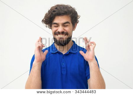 Excited Joyful Guy Keeping Fingers Crossed, Making Wish. Handsome Bearded Young Man In Blue Casual T