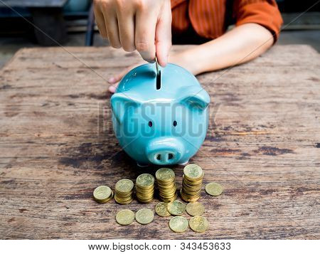 Business Woman Hand Putting Coin Into  Blue Piggy Bank With 
Gold Coins Pile Growth Graph, Saving Mo