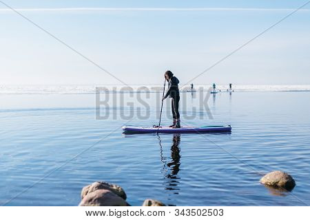 Attractive Caucasian Woman In Black Wetsuit Paddle On Sup Board With An Oar. Female Floating On Stan