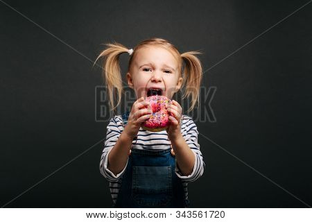 Happy cute boy is having fun played with donuts on black background wall. Bright photo of a boy. Colored donuts
