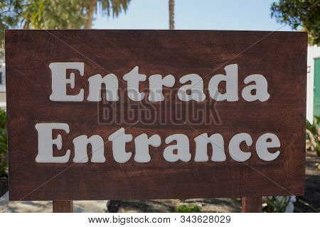The Spanish And English Word For -entrance- Written On A Big Wooden Sign
