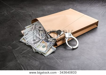 Envelope With Dollar Bills And Handcuffs On Grey Stone Table. Bribe Concept