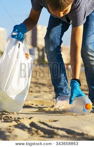 Cleaning City Beach From Plastic Trash. Kid Picking Up Plastic Bottle Trash From The Beach And Putti