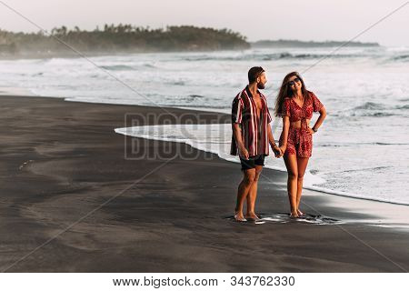 Happy Couple Holding Hands Walking On The Sandy Beach. Couple In Love At Sunset By The Sea. Couple I