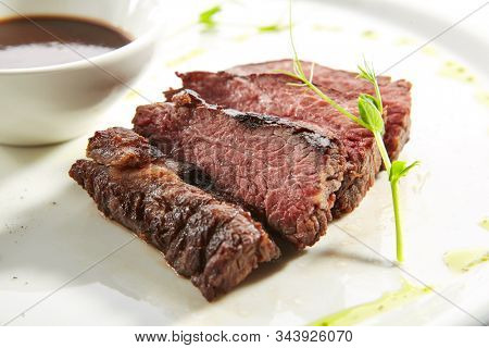 Alternative grilled skirt steak, well done machete fillet on white restaurant plate isolated. Macro shot of fresh juicy beef grillsteak, barbecue meat with brown spicy sauce and herbs closeup