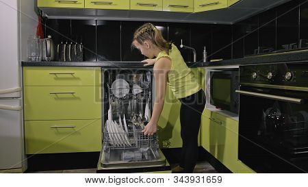 Smart Girl Learning To Use Dishwasher. Stylish Modern Built In Kitchen Appliances In Green Black. Ch