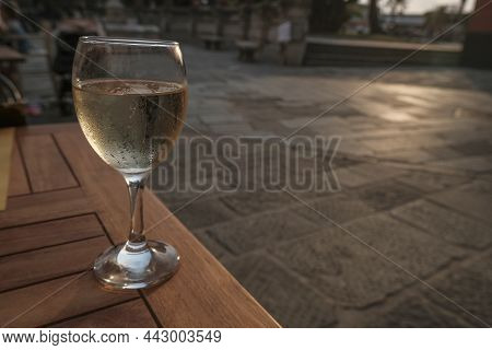 Misted Glass Of White Wine On The Terrace Close-up Across The Sunset City. Travel, Winemaking Indust