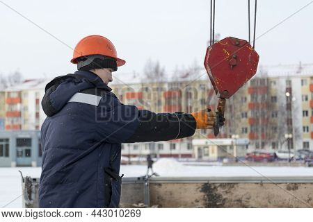 Portrait Of A Worker In A Blue Jacket With A Hood At The Hook Of A Truck Crane
