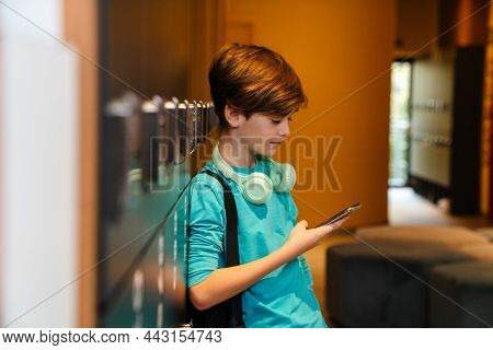 White ginger boy using mobile phone in checkroom at school