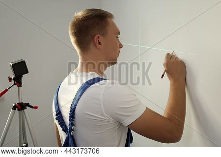 Worker Using Cross Line Laser Level And Pencil For Accurate Measurement On Light Wall