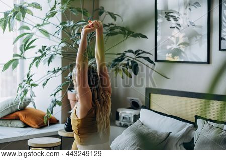 Woman With Blonde Hair Stretches Sitting On Bed And Looking At Window