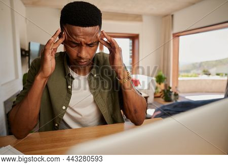 Exhausted Young Adult Black Male Massaging His Temples While He Works On Laptop From Home In Modern 