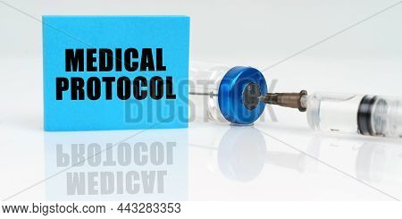 Medicine Concept. On A White Reflective Surface Are A Syringe, An Injection And A Blue Plaque That S