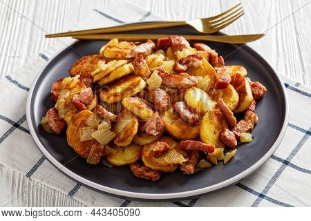 Close-up Of Bratkartoffeln, Fried Potatoes With Bacon And Onion On A Plate With Cutlery On A White W