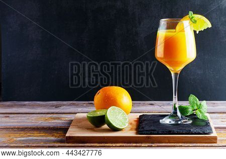 Glass Of Orange And Lime Juice With Mint On Wooden Table With Natural Orange And Lime Accompanying W