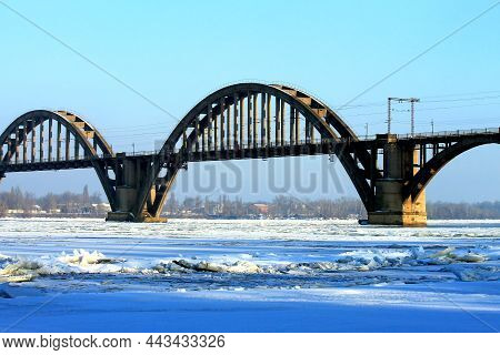 Arched Railway Bridge Over The River In Winter. A Beautiful Old Bridge, The Dnieper River Is Covered