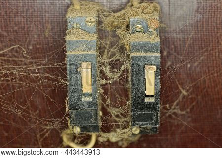 Two Old Black Plastic Toggle Switches On An Electric Meter In Gray Dust And Cobwebs On A Brown Wall