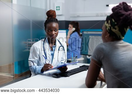 African American Therapist Discussing Sickness Symptoms Questionnaire With Sick Patient During Clini