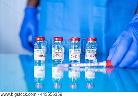 Close Up Of Doctor Placing Multiple Doses Of Covid-19 Or Coronavirus Vaccine And Syringe On Table Fo