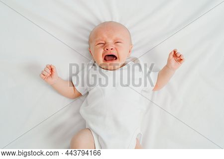 A Newborn Baby Cries On A White Sheet. Childish Tantrums. Top View.