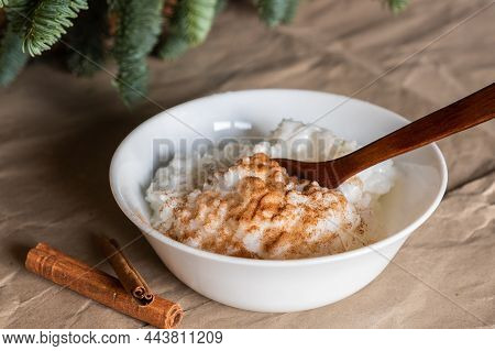 Traditional Scandinavian Rice Porridge And Cinnamon Sticks. Rice Pudding Is In A White Plate On Craf
