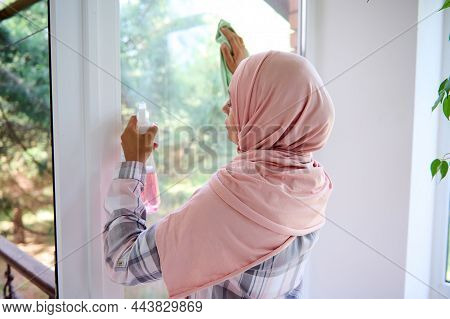 Rear View Of Arab Muslim Woman With Covered Head In Hijab Cleansing The Window, Removing Stains By S