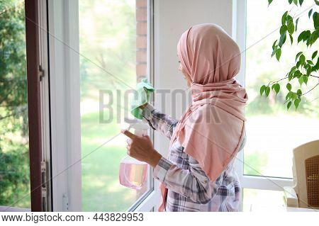 Arab Muslim Woman With Her Head Covered In A Hijab Washes Windows, Removes Stains, Sprays Detergent 