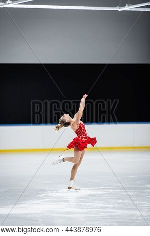 Full Length Of Happy Figure Skater With Raised Hands Doing Layback In Professional Ice Arena