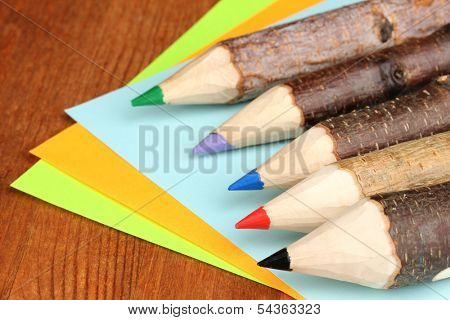 Colorful wooden pencils with sheets of paper on wooden table