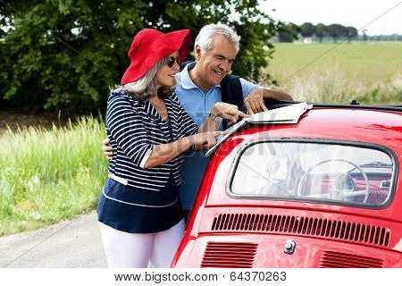 Senior couple watching a map with vintage car