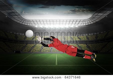 Fit goal keeper jumping up in a large football stadium with lights