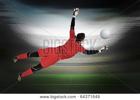 Fit goal keeper jumping up in a large football stadium with lights
